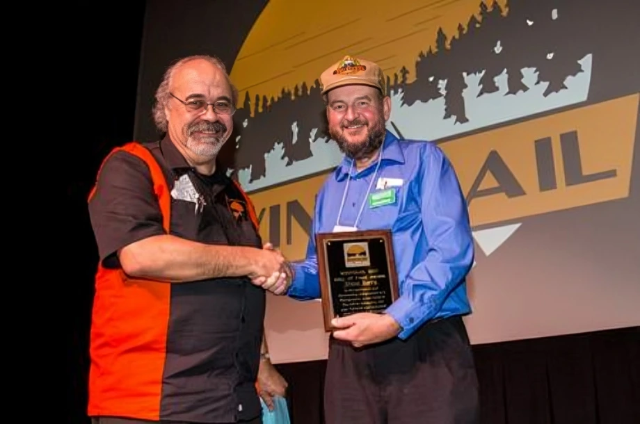 Two men shaking hands, holding an award.
