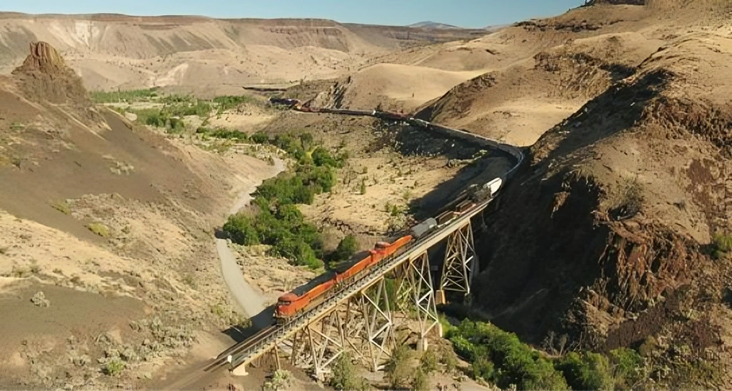 Train crossing bridge in desert landscape.