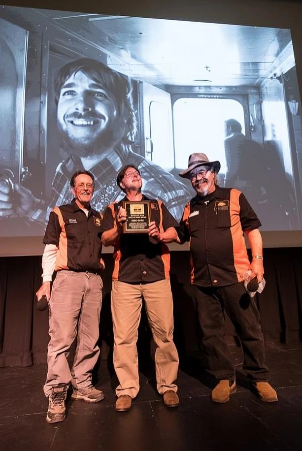 Three men with a plaque on stage.